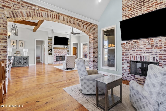 living area with built in features, arched walkways, crown molding, a fireplace, and light wood finished floors