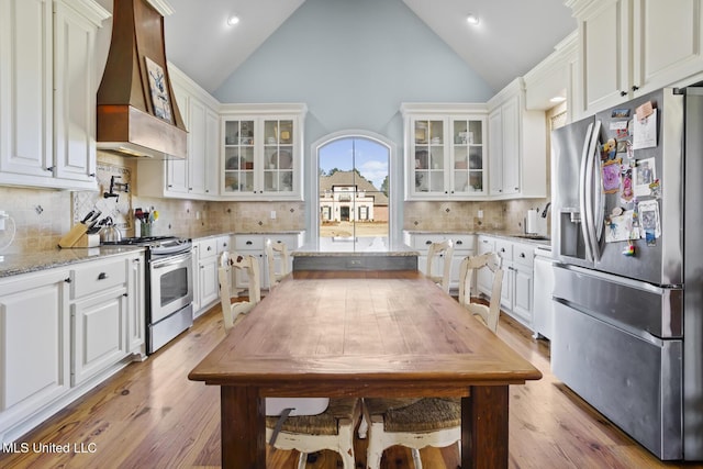 kitchen featuring stainless steel appliances, light stone counters, white cabinets, and custom range hood