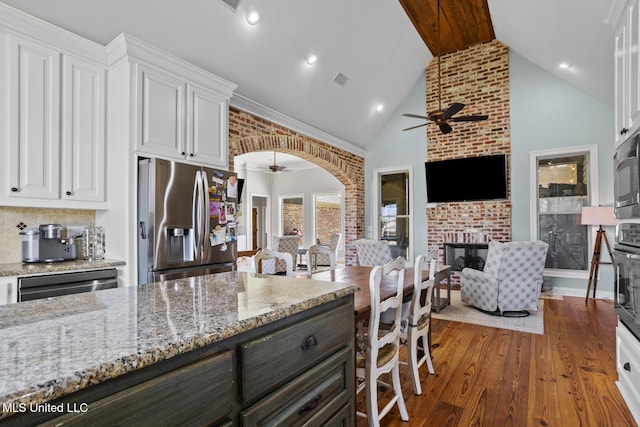 kitchen with white cabinetry, stainless steel fridge, a fireplace, and arched walkways