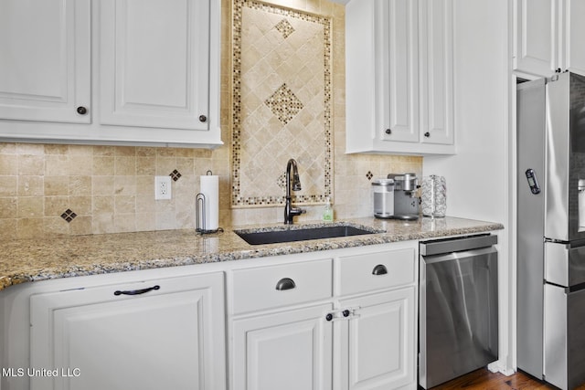 kitchen with stainless steel appliances, light stone counters, a sink, and white cabinets