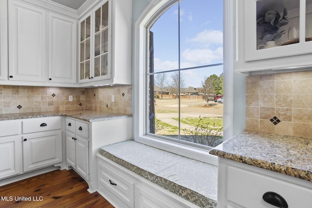 kitchen featuring tasteful backsplash, white cabinetry, glass insert cabinets, and light stone countertops