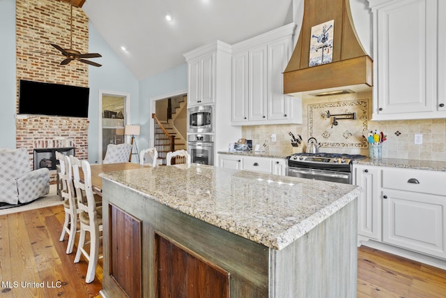 kitchen with a center island, custom exhaust hood, stainless steel appliances, light wood-type flooring, and white cabinetry