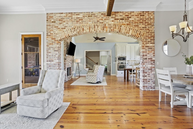 living room featuring light wood-type flooring, a fireplace, ornamental molding, and arched walkways