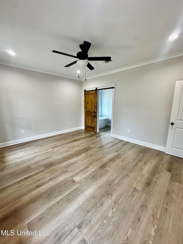 spare room with light hardwood / wood-style flooring, ornamental molding, a barn door, and ceiling fan