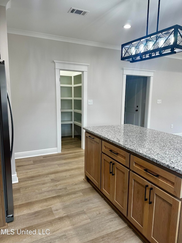 kitchen with ornamental molding, refrigerator, pendant lighting, light wood-type flooring, and light stone counters