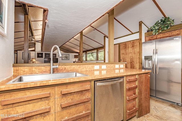 kitchen with vaulted ceiling, a sink, brown cabinetry, light countertops, and appliances with stainless steel finishes