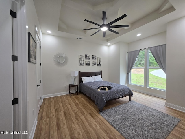 bedroom featuring recessed lighting, a raised ceiling, wood finished floors, visible vents, and baseboards