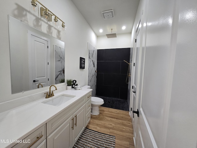 bathroom featuring recessed lighting, a tile shower, wood finished floors, toilet, and vanity