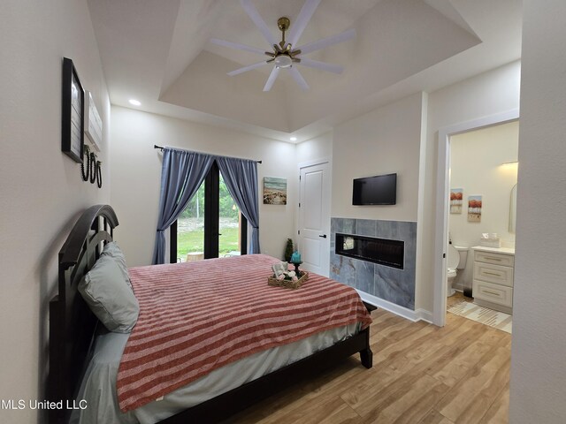 bedroom with light wood finished floors, recessed lighting, a tile fireplace, ensuite bath, and a raised ceiling