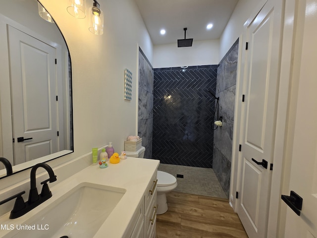 bathroom with tiled shower, wood finished floors, vanity, and toilet
