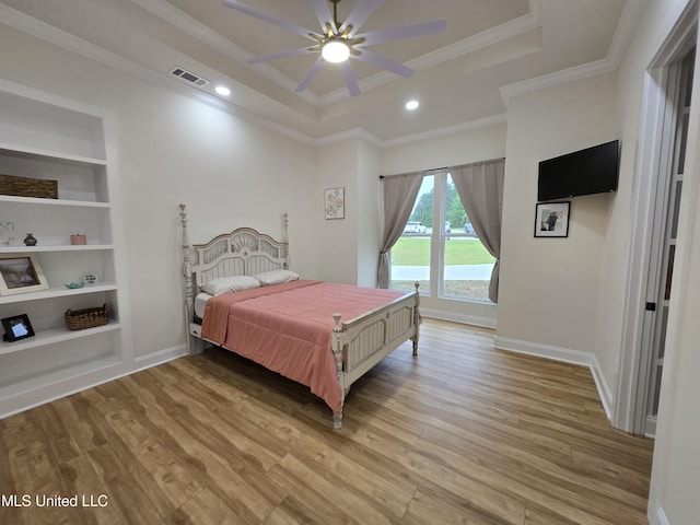 bedroom featuring crown molding, a tray ceiling, light wood finished floors, baseboards, and visible vents