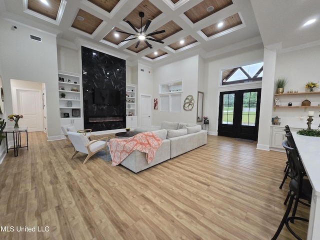 living room featuring a high ceiling, ornamental molding, coffered ceiling, and light wood-style flooring