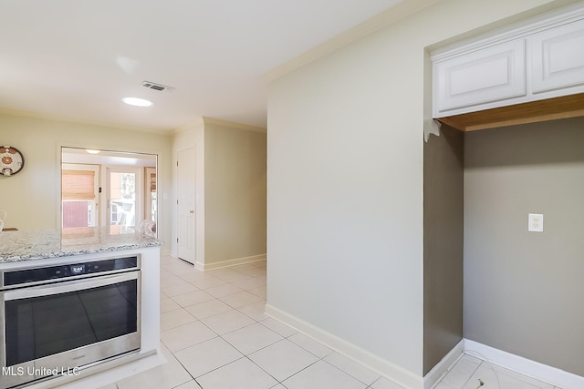 kitchen with light tile patterned flooring, crown molding, light stone countertops, oven, and white cabinets