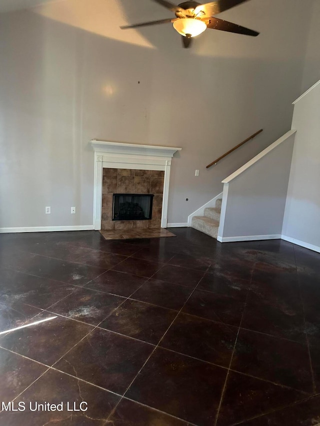 unfurnished living room featuring a tiled fireplace, ceiling fan, and dark tile patterned flooring