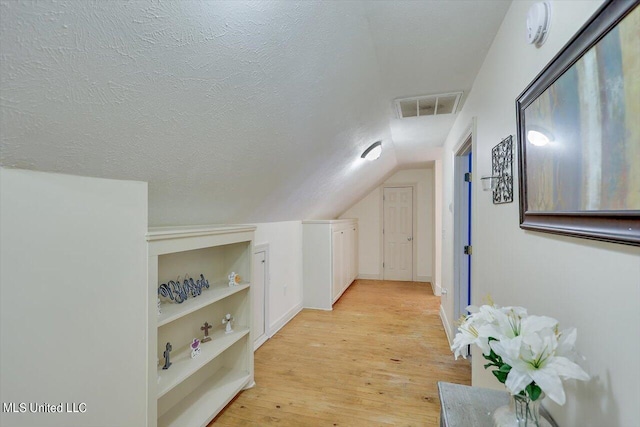 corridor featuring lofted ceiling, built in features, a textured ceiling, and light hardwood / wood-style floors