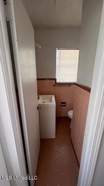 half bath with wainscoting, vanity, toilet, and tile walls