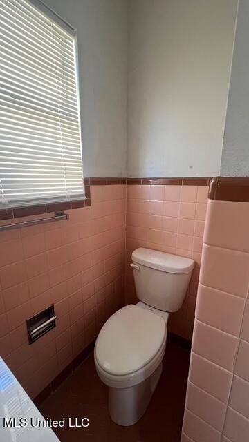 bathroom featuring a wainscoted wall, a healthy amount of sunlight, toilet, and tile walls