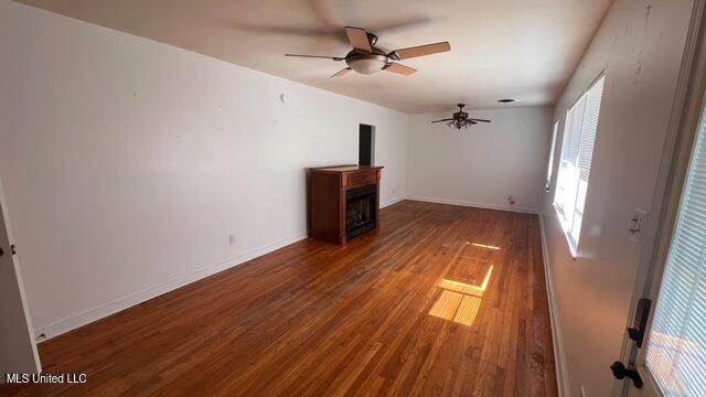 unfurnished living room with wood finished floors, a fireplace, baseboards, and ceiling fan