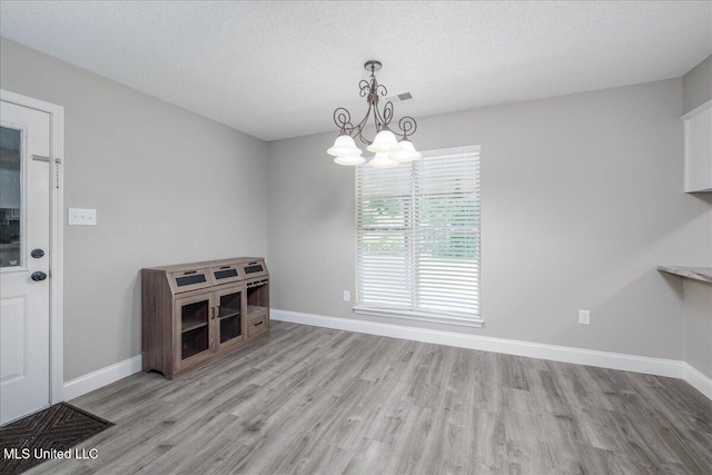 6967 Green Way Cv, Olive Branch, MS 38654 - unfurnished dining area featuring light wood finished floors, a chandelier, and a textured ceiling