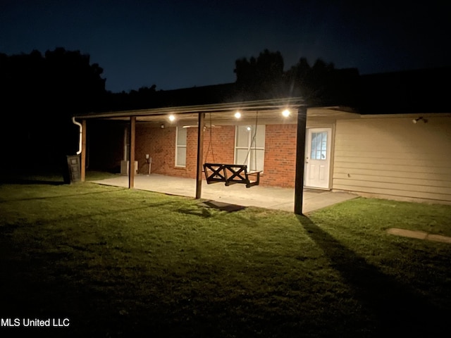 6967 Green Way Cv, Olive Branch, MS 38654 - back of house at night featuring a patio area, brick siding, and a lawn