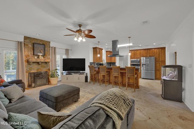 living room with ceiling fan, a stone fireplace, and ornamental molding