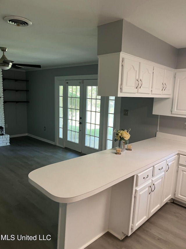 kitchen with kitchen peninsula, wood-type flooring, crown molding, white cabinetry, and ceiling fan