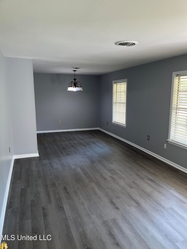 empty room with a notable chandelier and dark hardwood / wood-style flooring