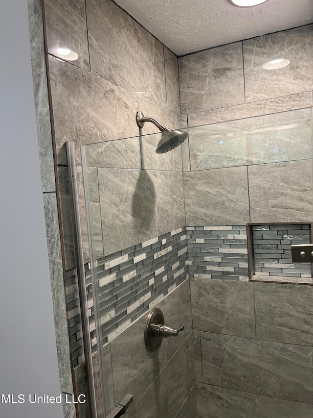 bathroom with a textured ceiling and tiled shower