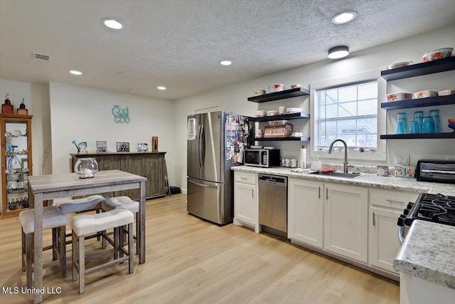 kitchen featuring light wood-style flooring, appliances with stainless steel finishes, open shelves, and a sink