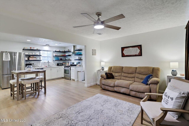 living area featuring a textured ceiling, ceiling fan, light wood finished floors, and indoor wet bar