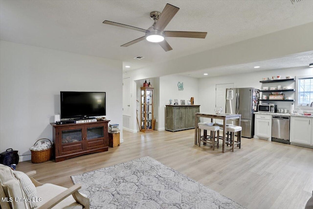 living area featuring a textured ceiling, recessed lighting, visible vents, a ceiling fan, and light wood finished floors