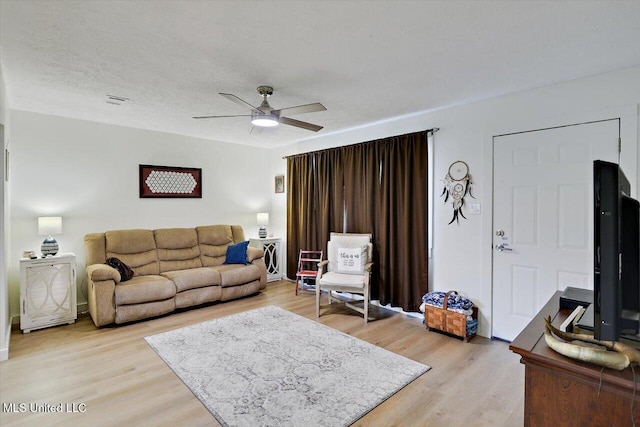 living room featuring light wood-type flooring, ceiling fan, and a textured ceiling