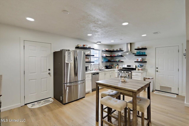 kitchen with stainless steel appliances, light countertops, light wood-type flooring, wall chimney range hood, and open shelves