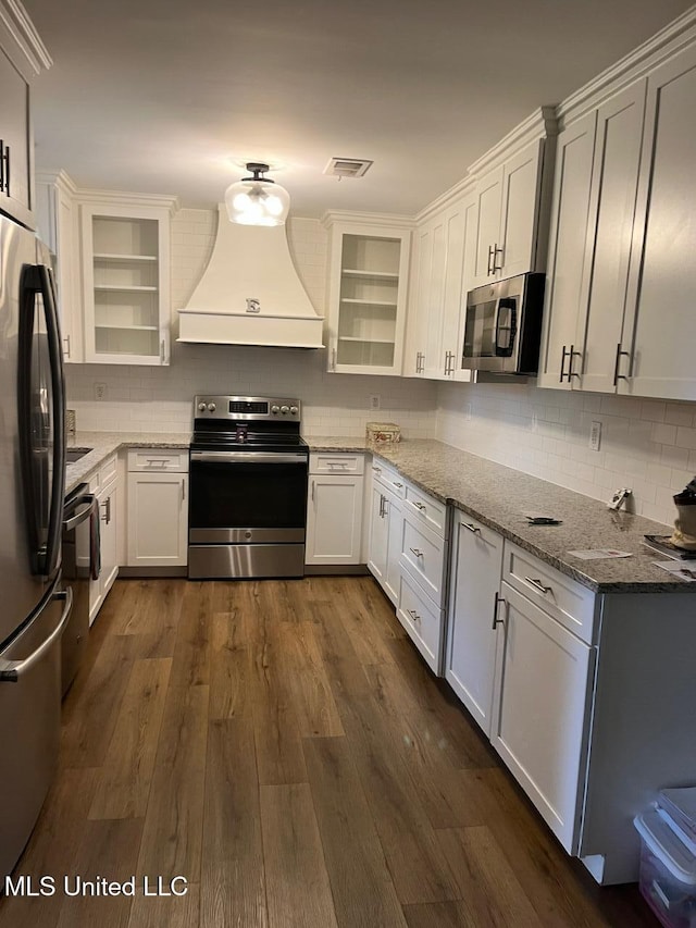 kitchen with dark wood-style floors, tasteful backsplash, custom range hood, appliances with stainless steel finishes, and light stone countertops