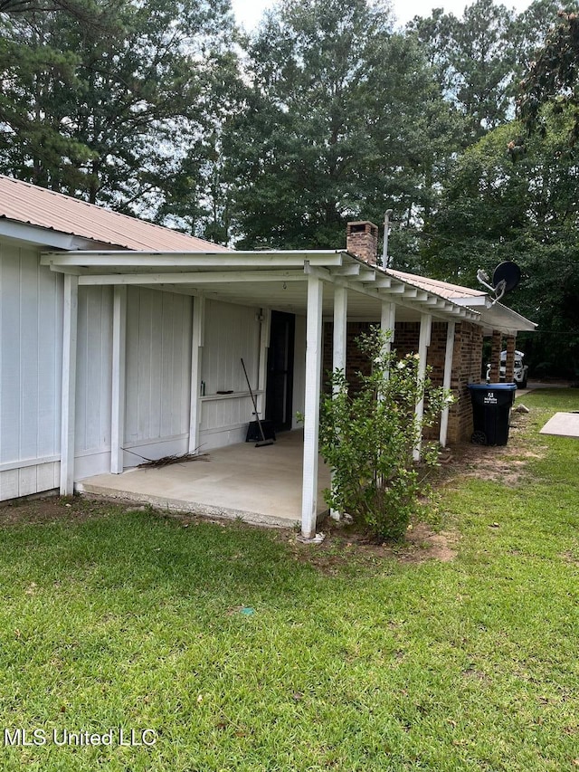 view of side of home with metal roof, a yard, a chimney, and a patio