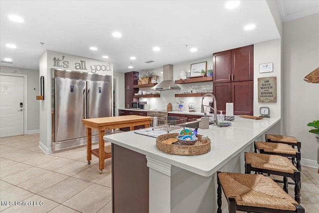 kitchen featuring kitchen peninsula, light tile patterned flooring, sink, wall chimney exhaust hood, and stainless steel appliances