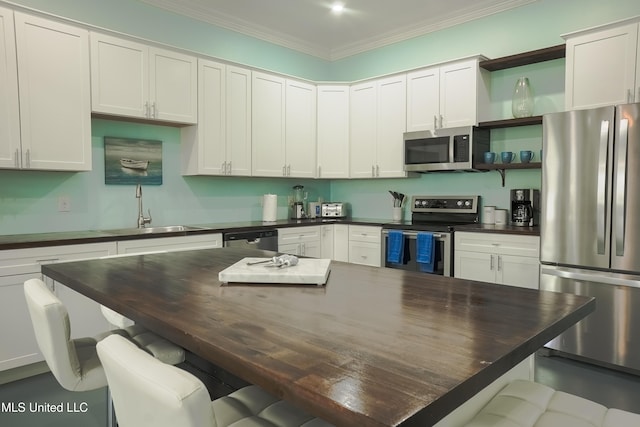 kitchen with a breakfast bar area, stainless steel appliances, a sink, white cabinetry, and ornamental molding