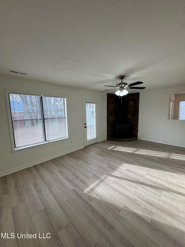 unfurnished living room with ceiling fan, a healthy amount of sunlight, a textured ceiling, and light wood-type flooring