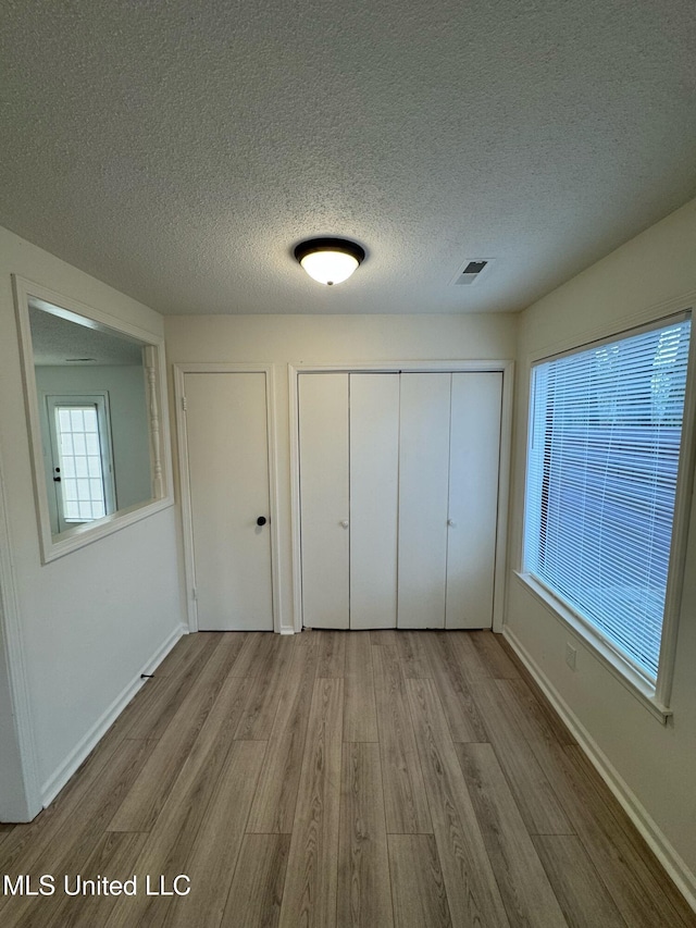 unfurnished bedroom featuring a closet, a textured ceiling, and light wood-type flooring