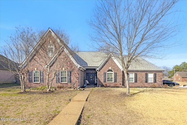 view of front of home featuring a shingled roof, brick siding, and a front lawn