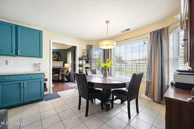 dining room featuring visible vents, a fireplace, a textured ceiling, and light tile patterned flooring