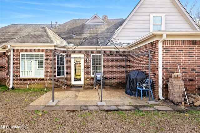 rear view of property featuring roof with shingles, a patio, and brick siding