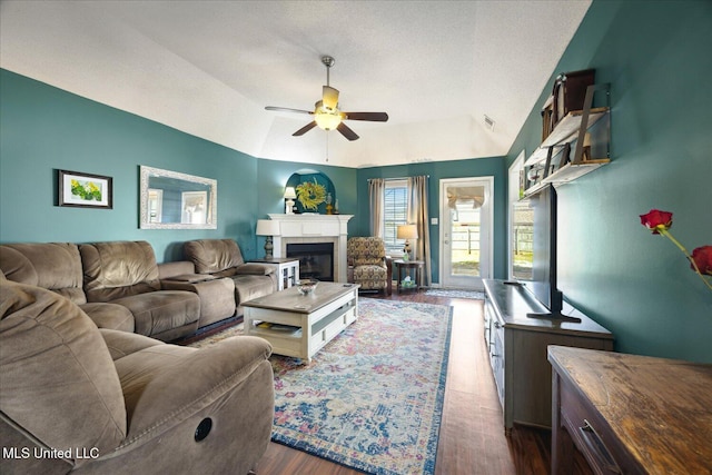 living room featuring vaulted ceiling, dark wood-type flooring, a glass covered fireplace, and a ceiling fan