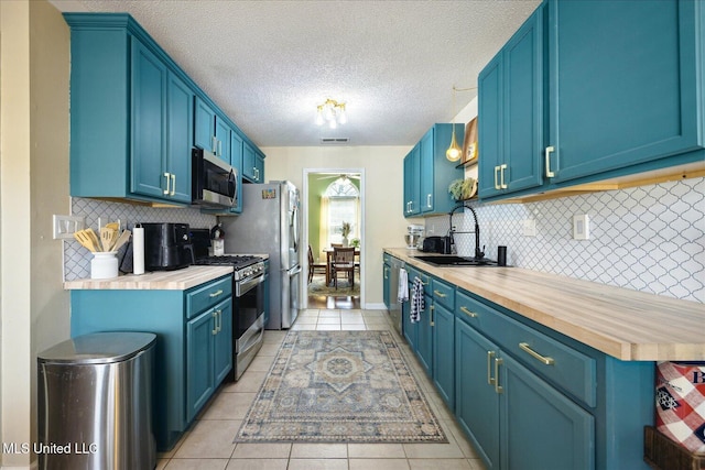 kitchen featuring light tile patterned floors, visible vents, appliances with stainless steel finishes, blue cabinets, and a sink