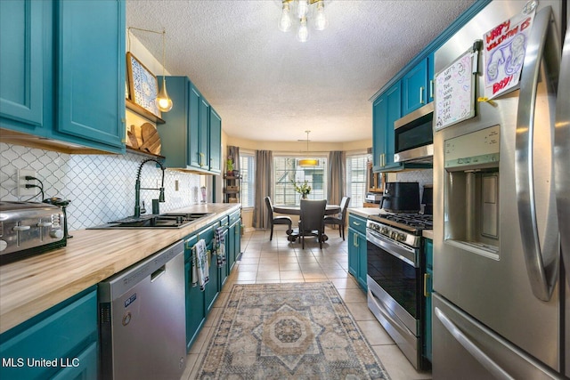 kitchen featuring light tile patterned floors, blue cabinets, butcher block counters, a sink, and appliances with stainless steel finishes