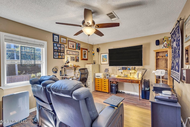 living room featuring ceiling fan, a textured ceiling, and light wood-type flooring