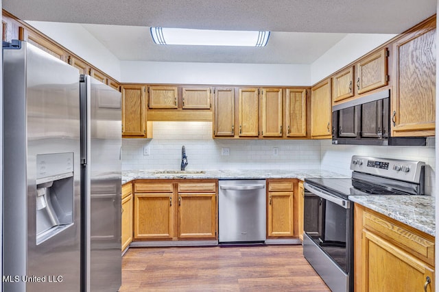 kitchen with hardwood / wood-style floors, tasteful backsplash, light stone counters, appliances with stainless steel finishes, and sink