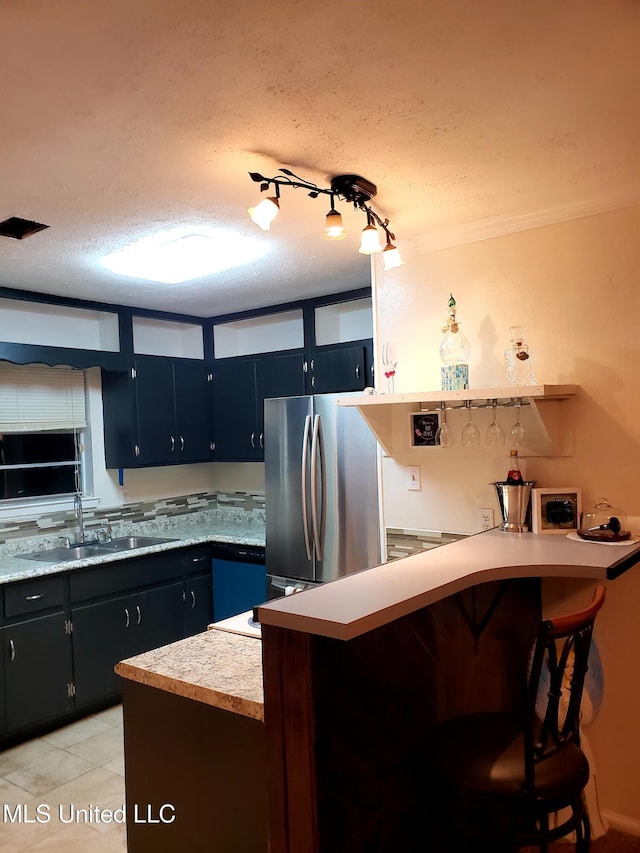 kitchen featuring a kitchen bar, a textured ceiling, stainless steel refrigerator, and sink