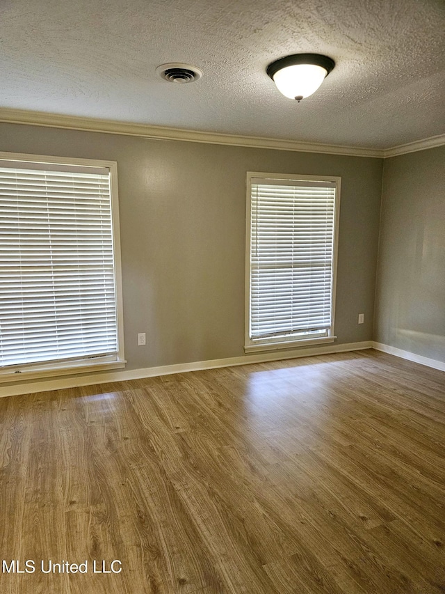 spare room with crown molding, wood finished floors, visible vents, and a textured ceiling
