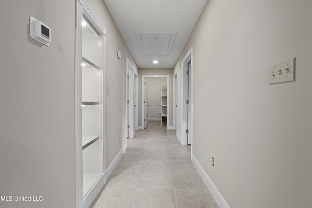 corridor featuring light tile patterned flooring, baseboards, and attic access